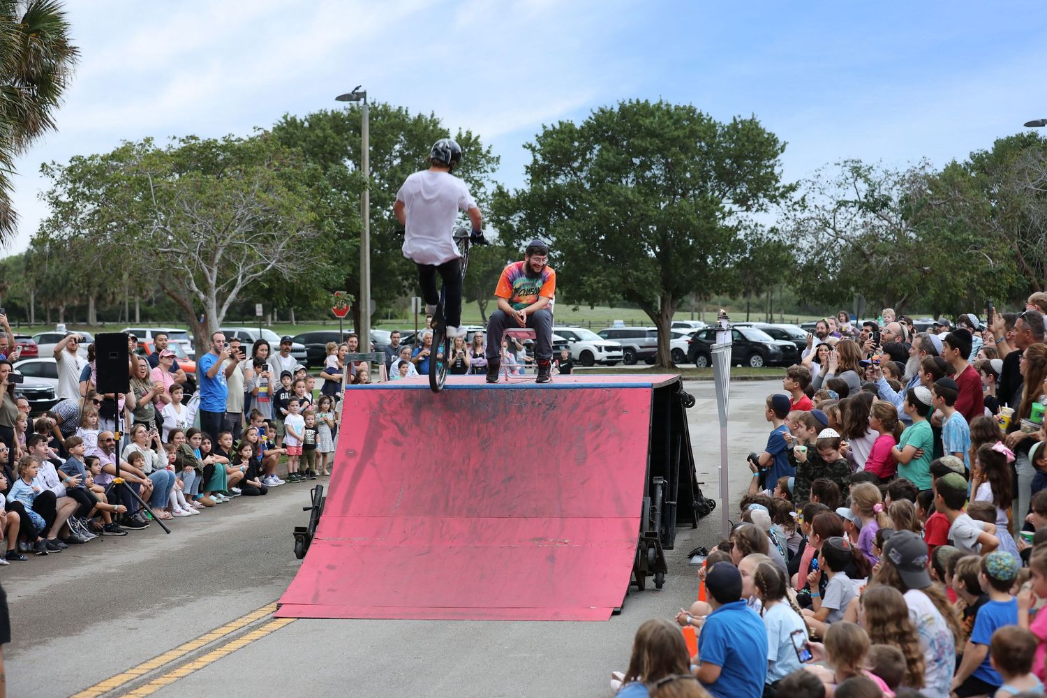 Skateboarder performs on a pink halfpipe ramp before a large crowd at an outdoor skate park event.