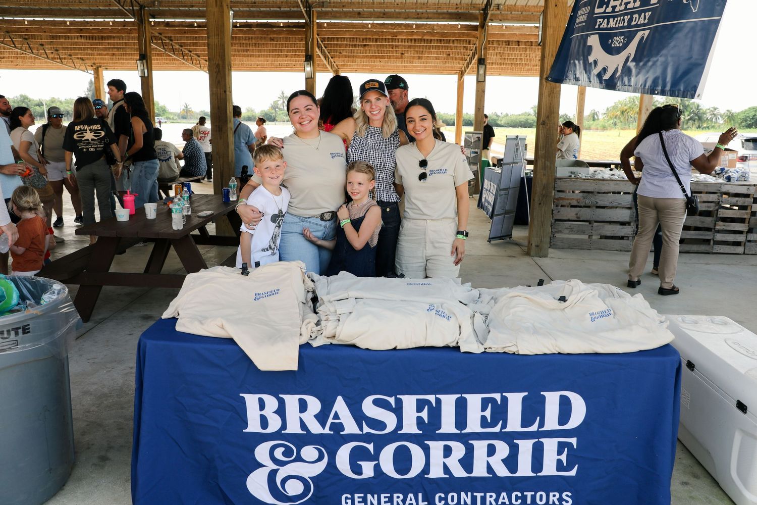 Group of people smiling behind a Brasfield & Gorrie General Contractors branded table at an outdoor event.