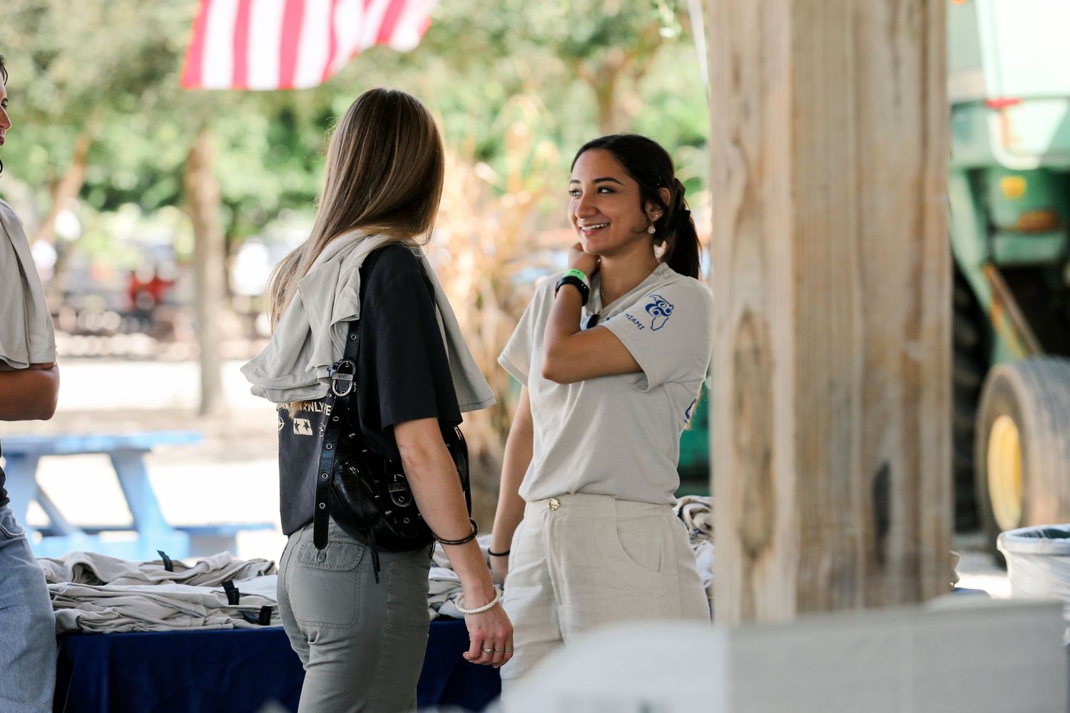 Two women in casual attire engage in conversation outdoors at a community event near a table.