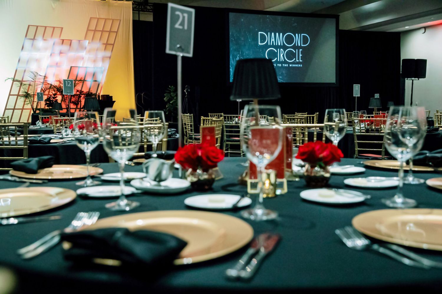 Elegant Diamond Circle gala dinner table setting with gold chargers, crystal glasses, and red floral centerpieces in a ballroom.