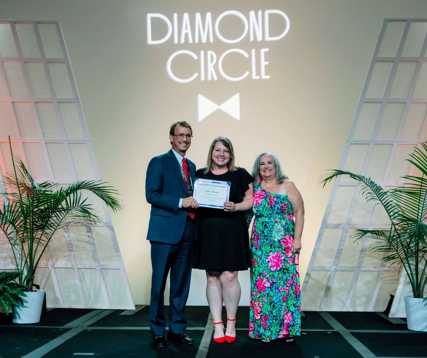 Three people posing with a certificate in front of a Diamond Circle event backdrop at an awards ceremony.