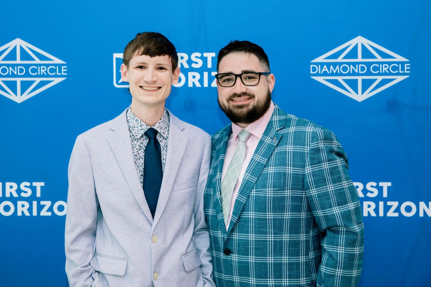 Two men in suits pose smiling at a First Horizon Diamond Circle event in front of a blue branded backdrop.