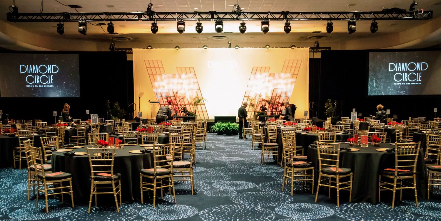 Elegant Diamond Circle Awards banquet hall with round tables, gold chairs, and dual projection screens in a grand venue.