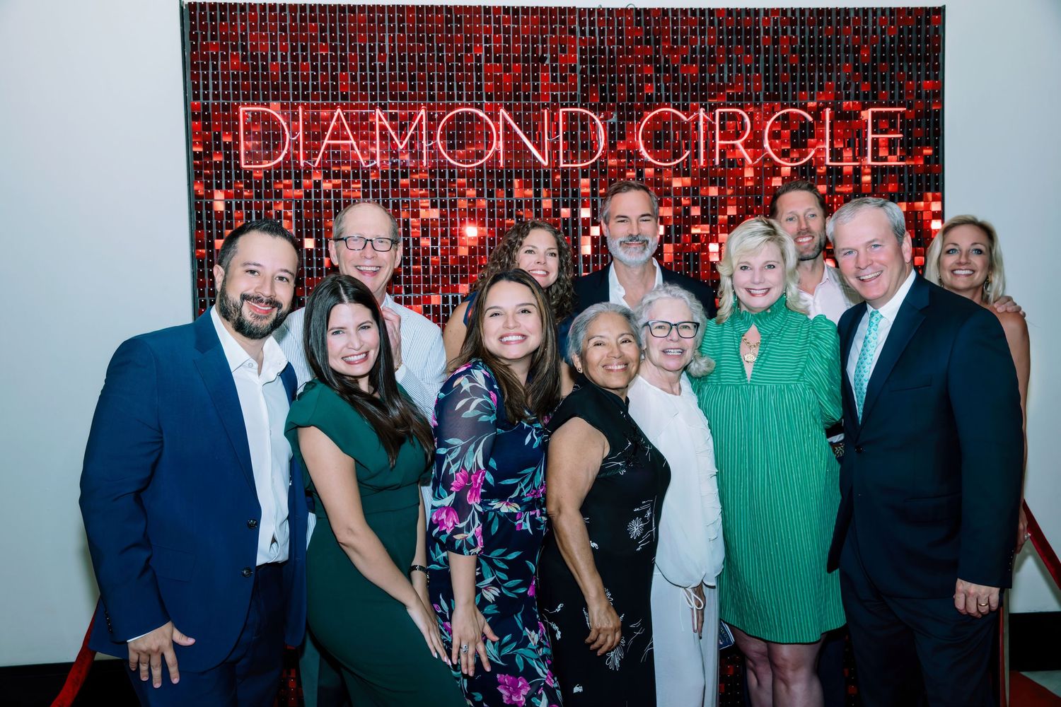 Group of smiling professionals posing together at a Diamond Circle gala event in front of a red and black logo wall.