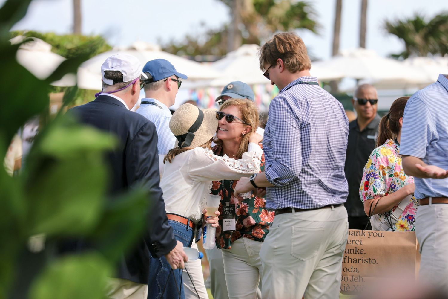 Guests socializing at an outdoor event on a sunny day, with palm trees and a beachside backdrop.