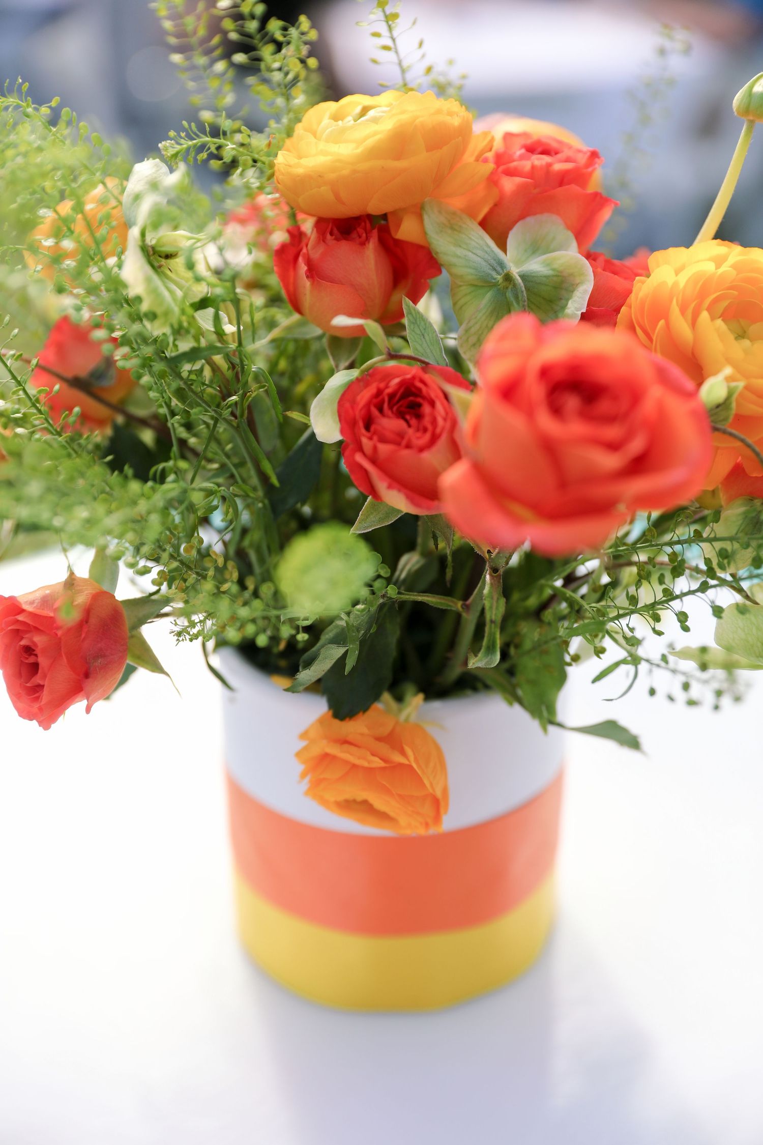 Vibrant orange and yellow roses in a candy corn striped vase centerpiece on a white table.
