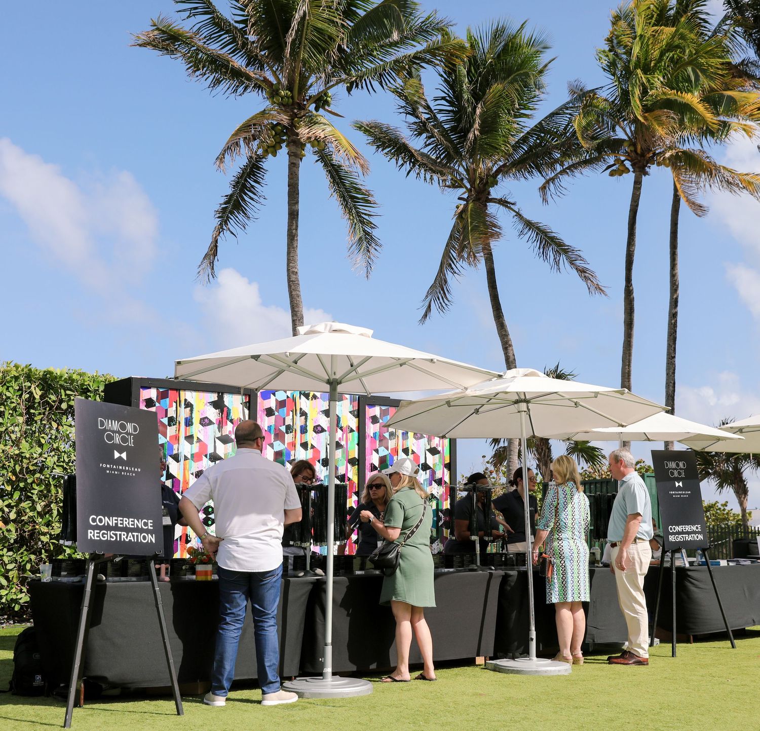 Outdoor conference registration booth with white umbrellas and palm trees at a tropical resort venue.