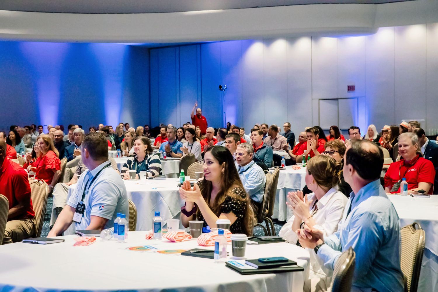 Large audience seated at round tables during a corporate conference event in a modern ballroom.