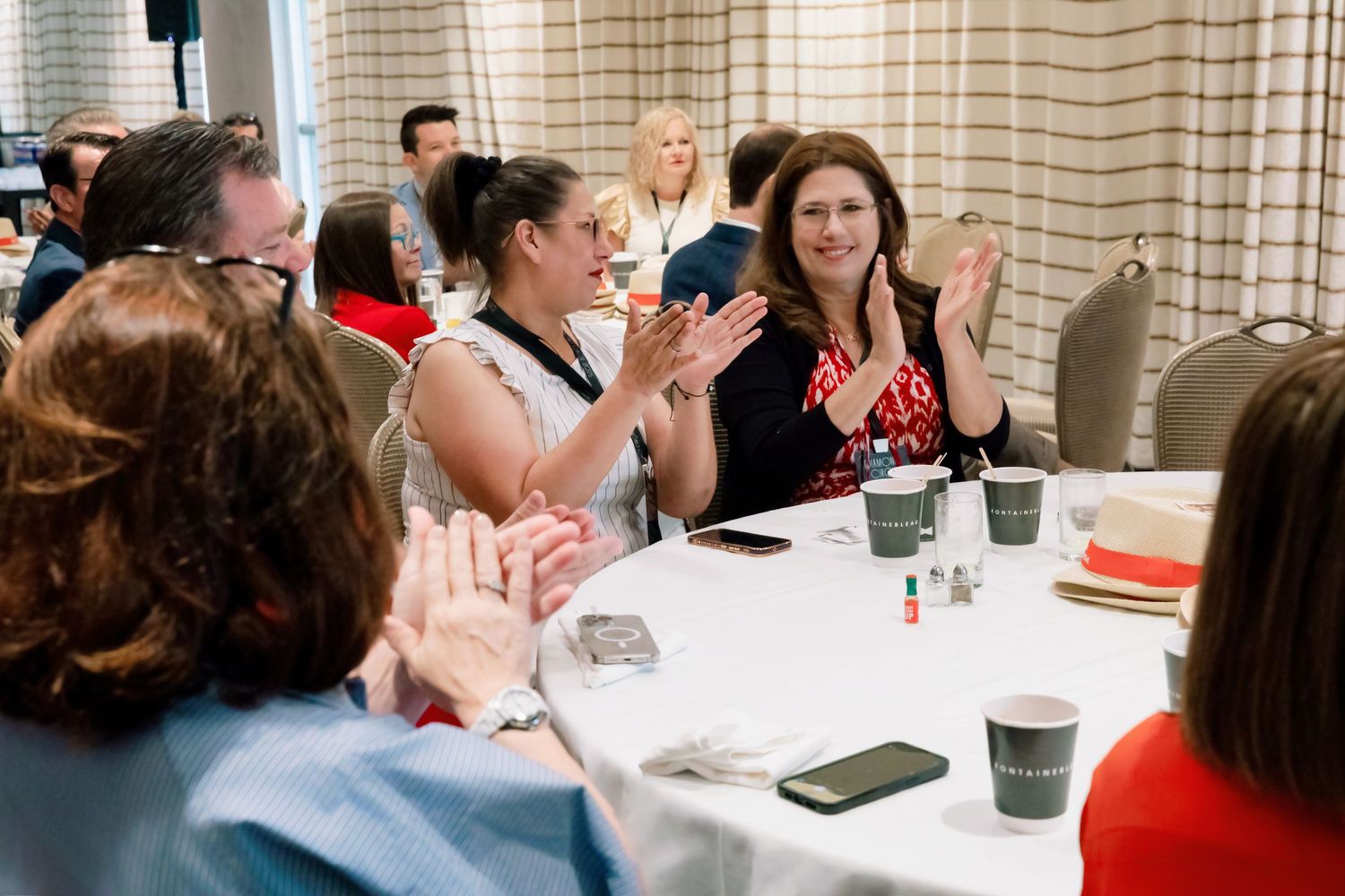 Group of professionals applauding at a round table during a business conference meeting in a hotel ballroom.