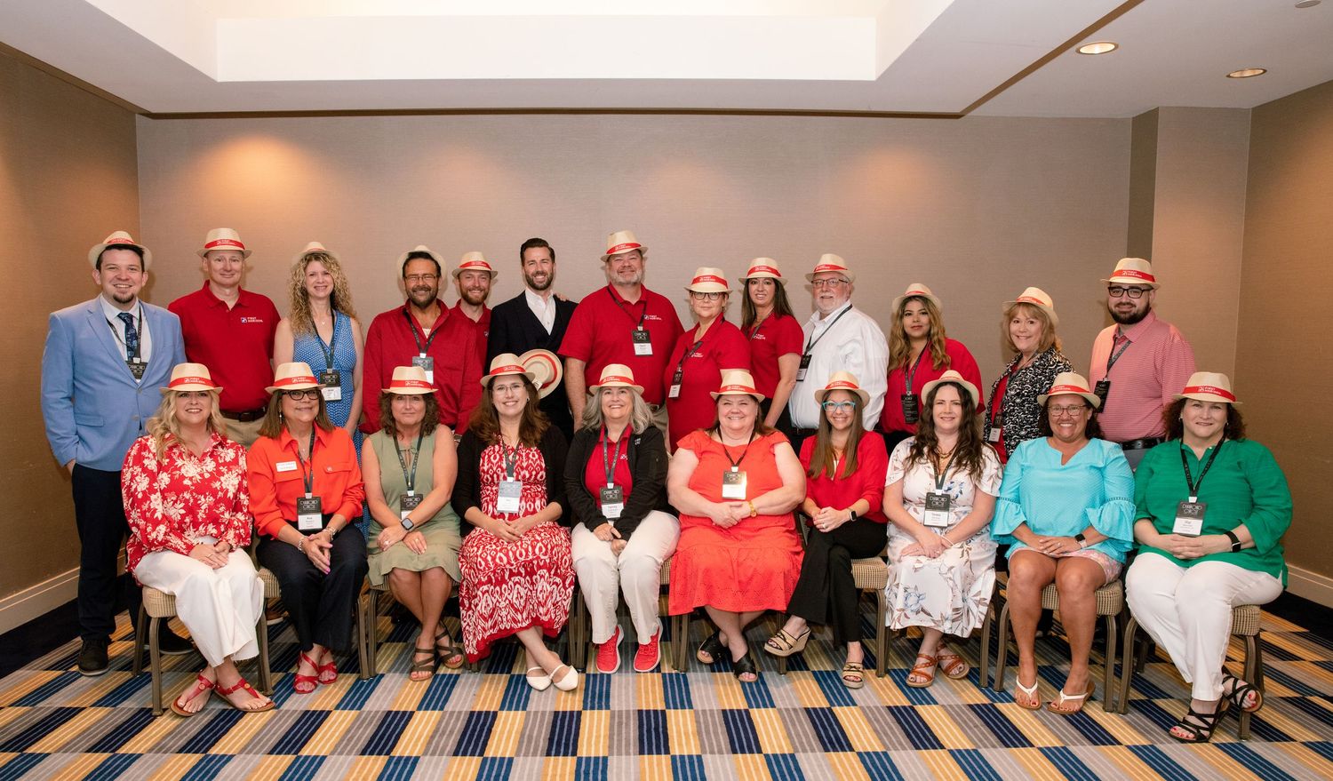 Large group of professionals in festive hats posing for a formal group photo in a conference room.