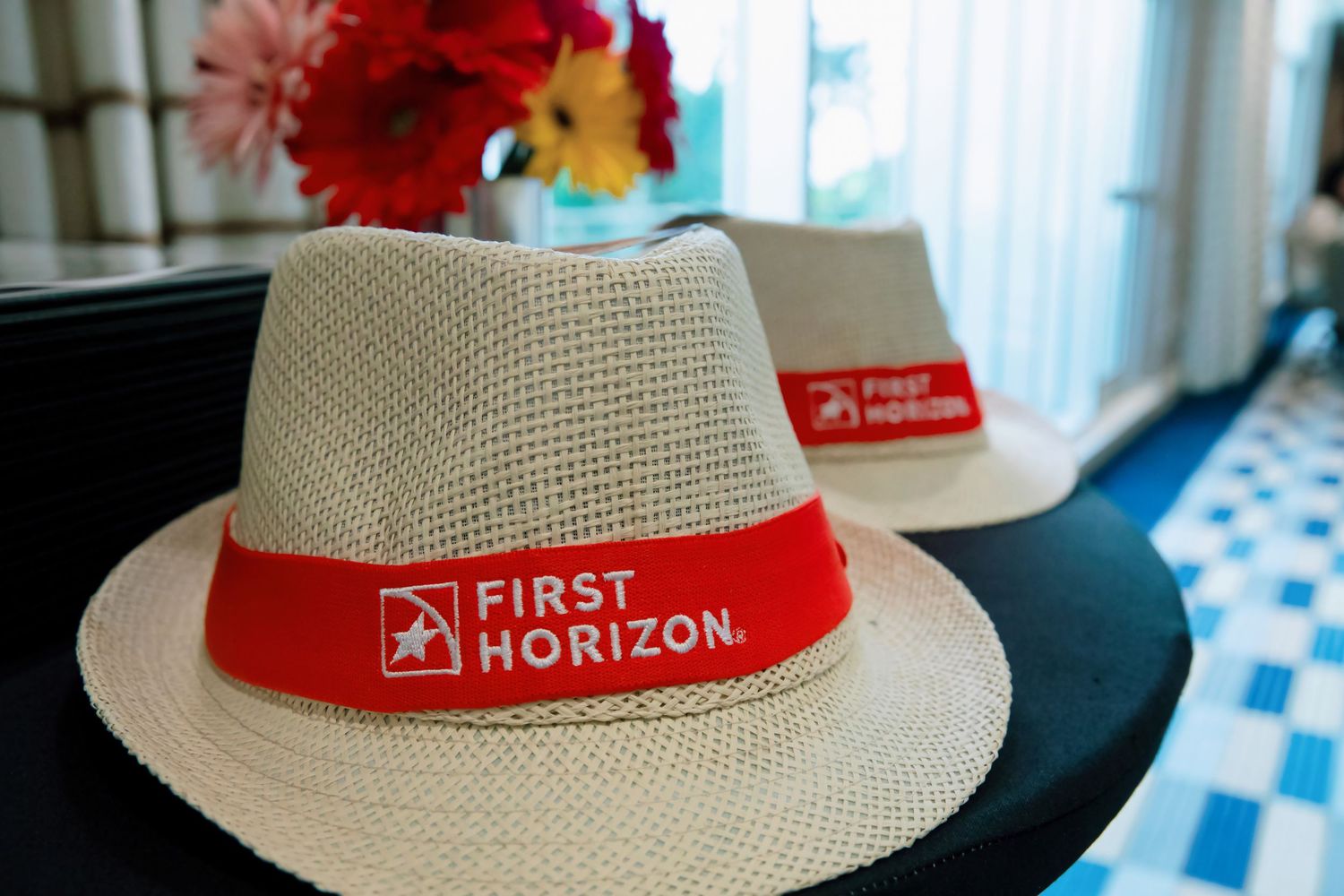 Two First Horizon branded straw fedora hats with red bands displayed on a table at an event.