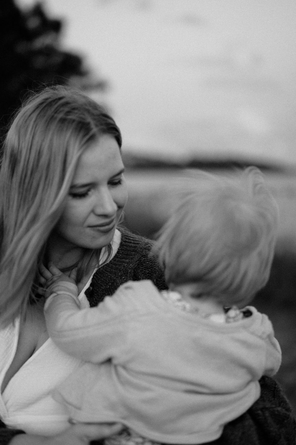 Black and white photo of a smiling blonde woman tenderly holding a young child outdoors.