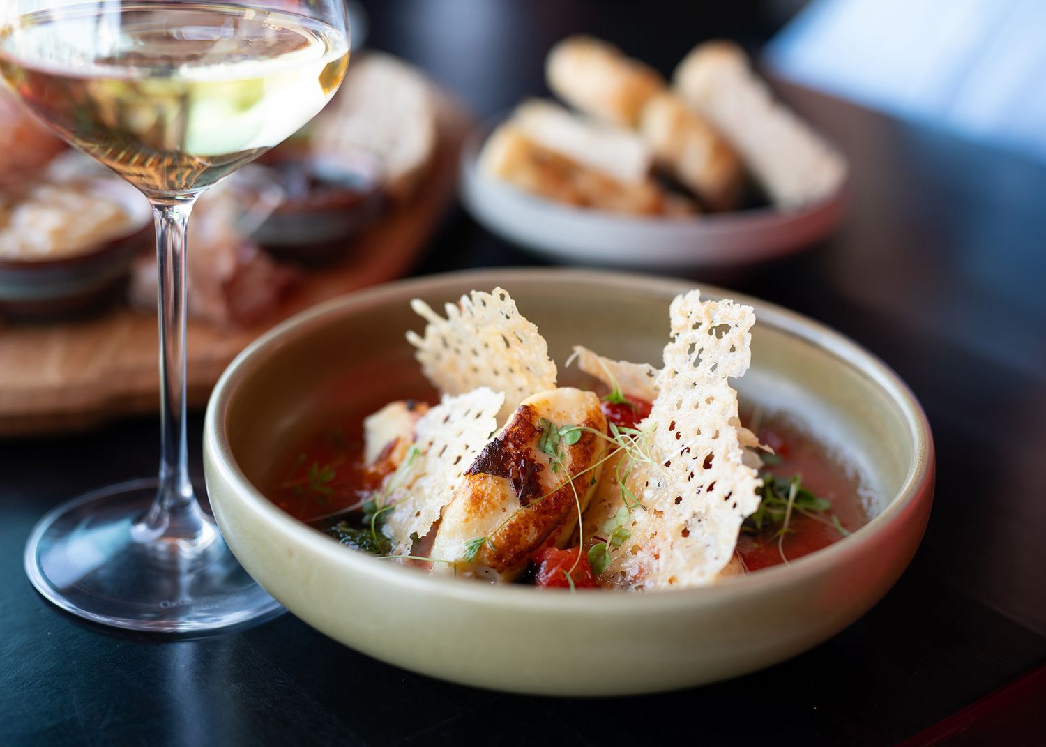 Elegant restaurant dish with crispy parmesan crisps, tomato sauce, and herbs served alongside a glass of white wine.