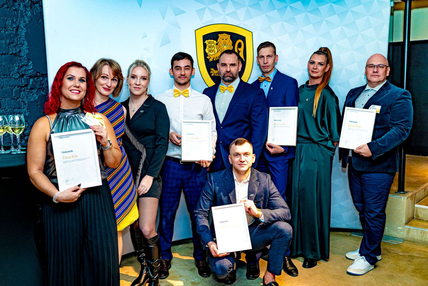 Group of professionals holding certificates at a formal award ceremony in front of a yellow emblem backdrop.