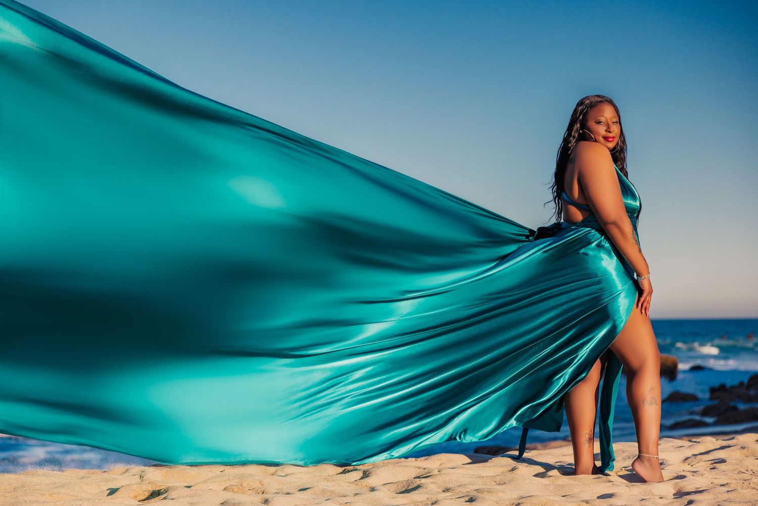 Couple embracing on beach at sunset, woman in purple flowing gown.