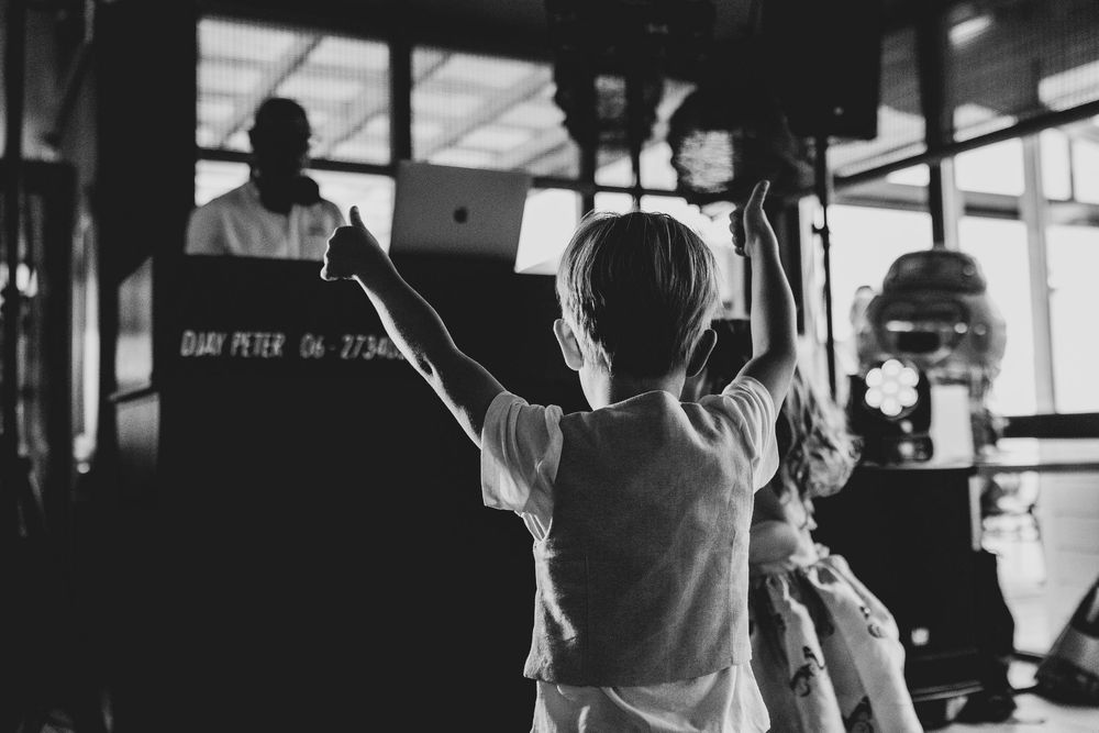 Child raises hand at a DJ booth in a black and white photo at an indoor event.