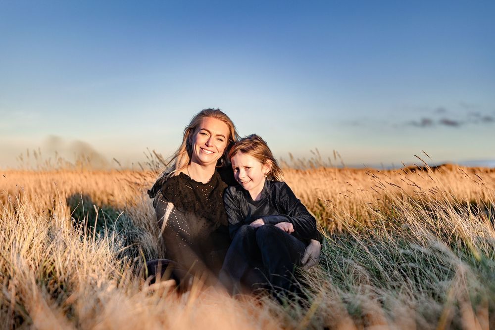 Two smiling females sit together in golden grass field during warm sunset light outdoors.