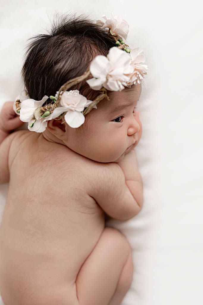 Professional Temecula newborn photographer photo of baby girl lying on white blanket wearing a delicate floral crown.