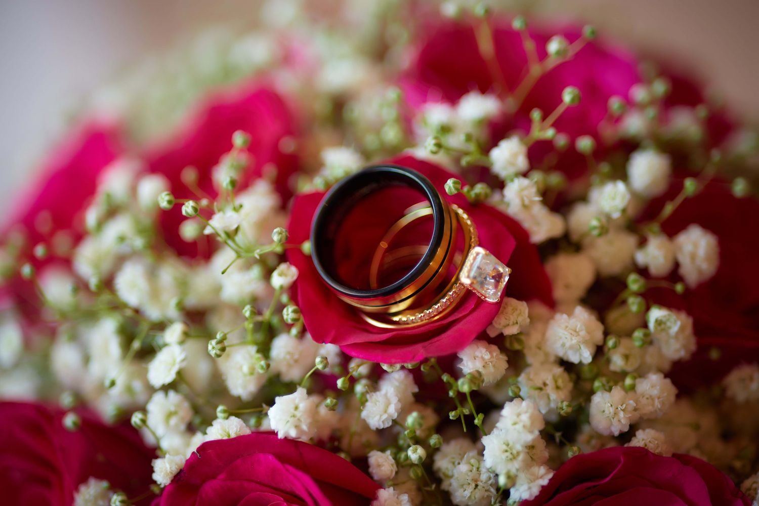 Gold wedding rings resting on a bridal bouquet of pink roses and white baby's breath flowers.