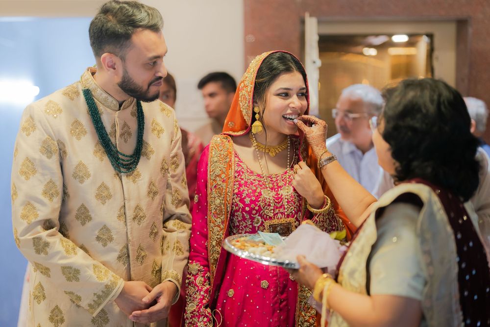 Indian bride in red lehenga and groom in cream sherwani sharing a joyful moment during traditional wedding ceremony.