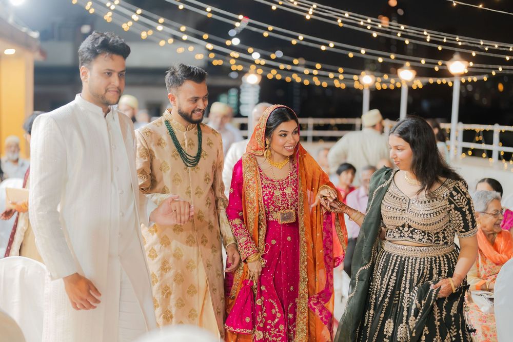 South Asian wedding guests in traditional attire including vibrant pink lehenga and golden sherwani under festive string lights.