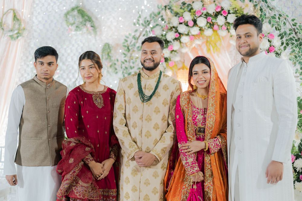 A group of five people in traditional South Asian wedding attire posing together in front of a floral backdrop.