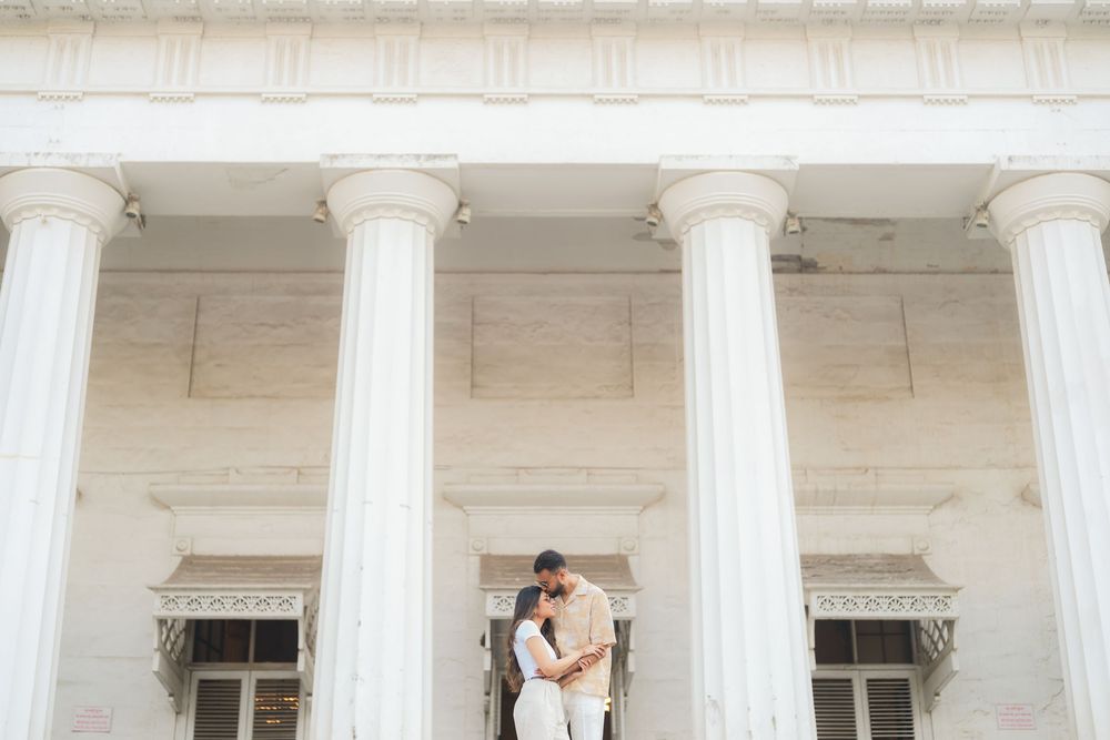 Couple embracing romantically between white Greek Revival columns at a grand neoclassical building.