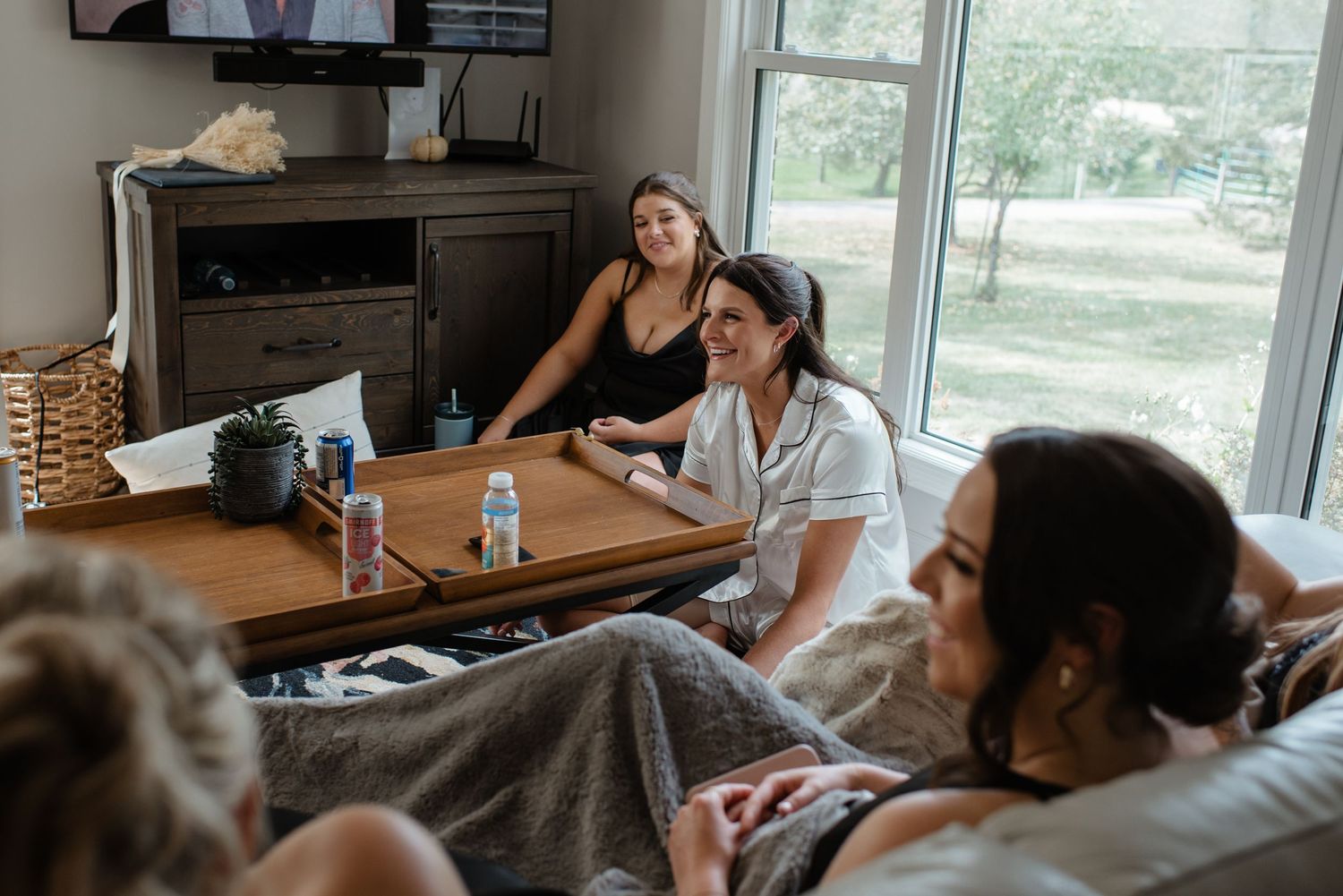 Three women relaxing together in a cozy living room, smiling and chatting near a wooden coffee table.