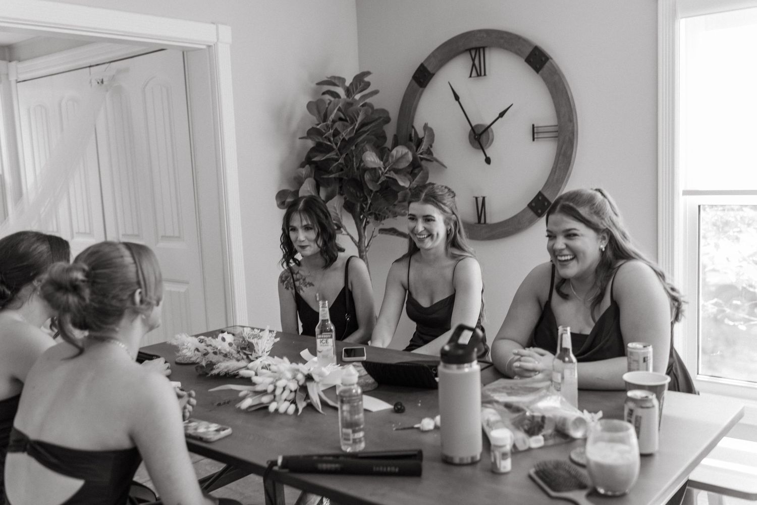 Black and white photo of bridesmaids laughing together at a table during wedding preparations.