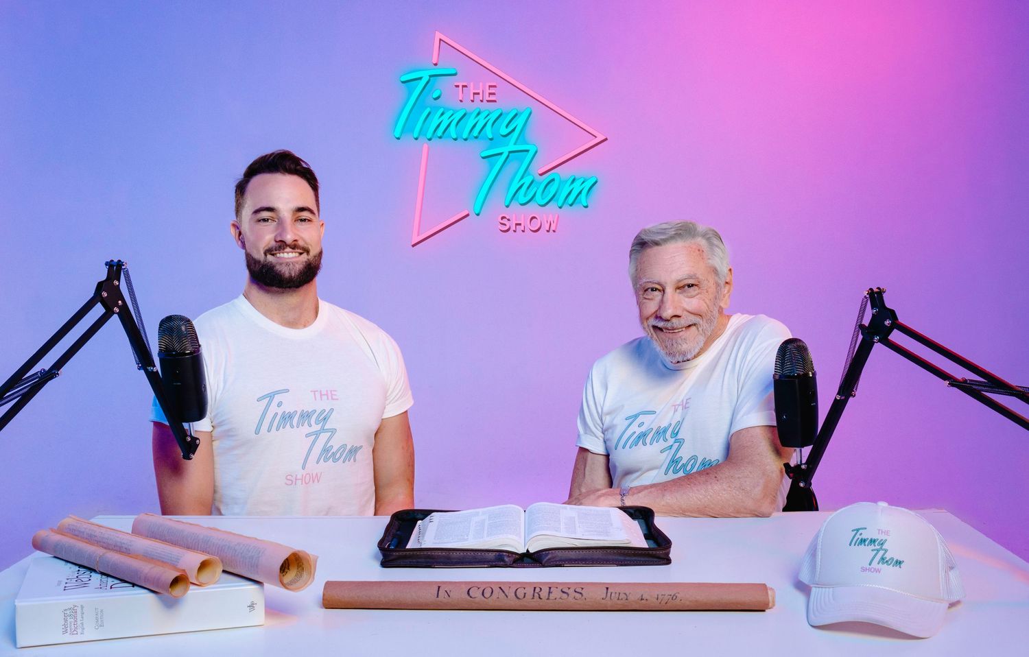 Two men hosting The Timmy Thorn Show podcast, sitting at a desk with microphones, books, and branded merchandise.