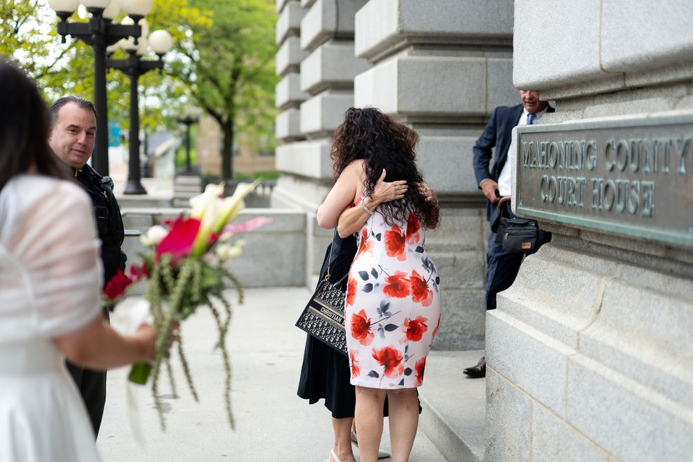 Wedding couple embracing outside Hennepin County Courthouse with flowers.