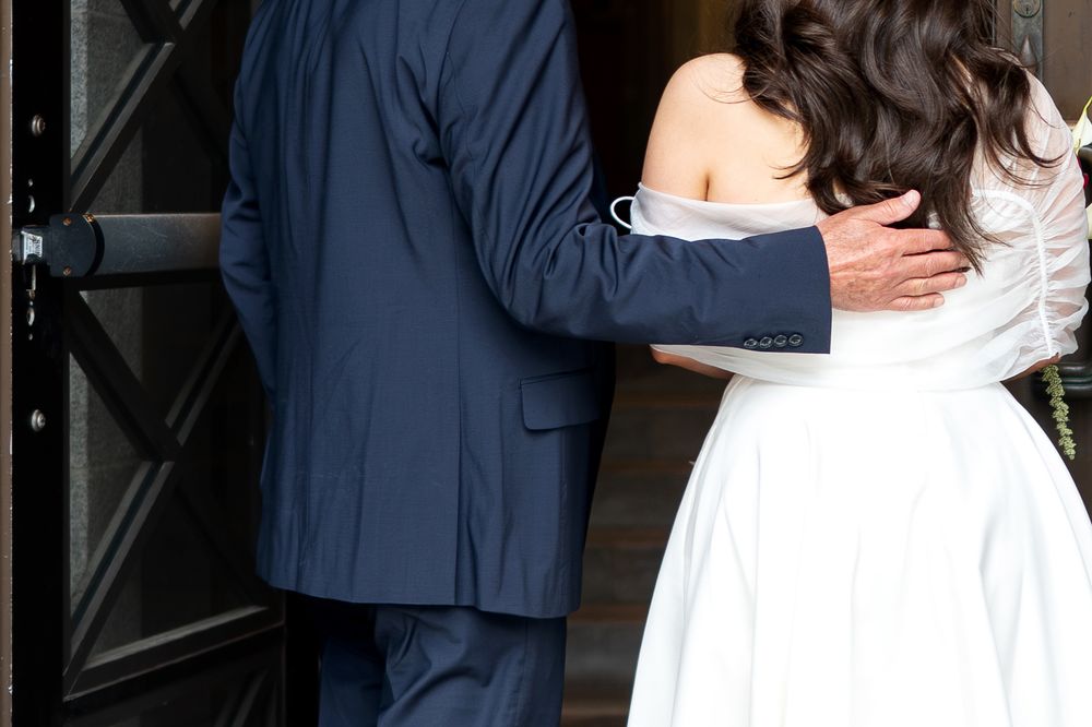 Couple embraces at ornate dark wooden door, groom in navy suit.