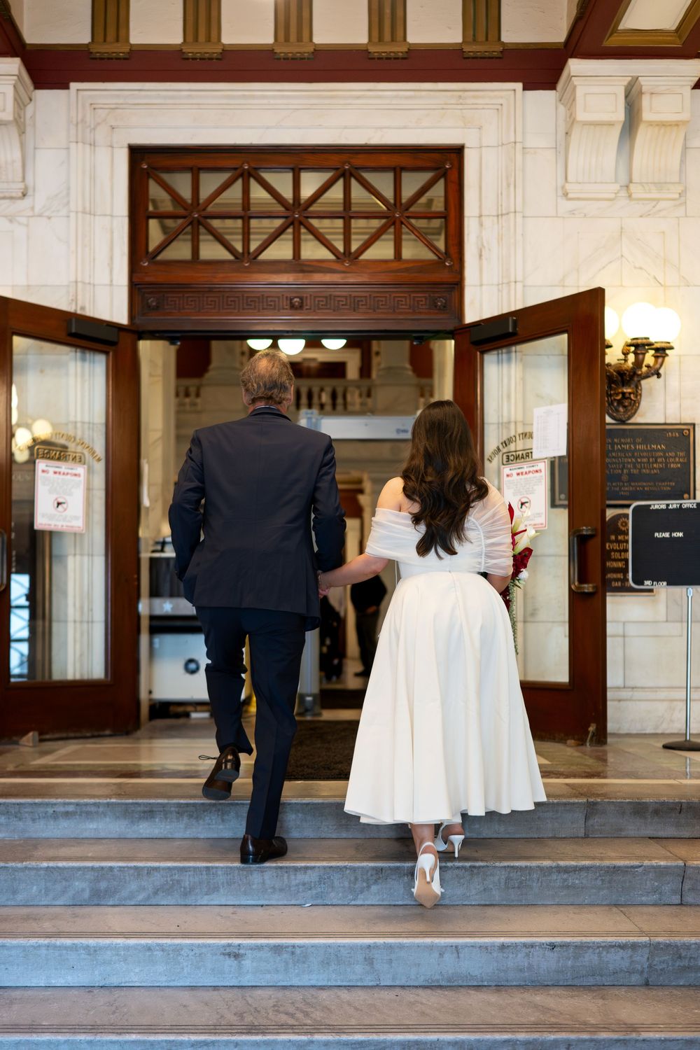 Bride and groom walking hand in hand up marble steps into an elegant courthouse for their wedding ceremony.