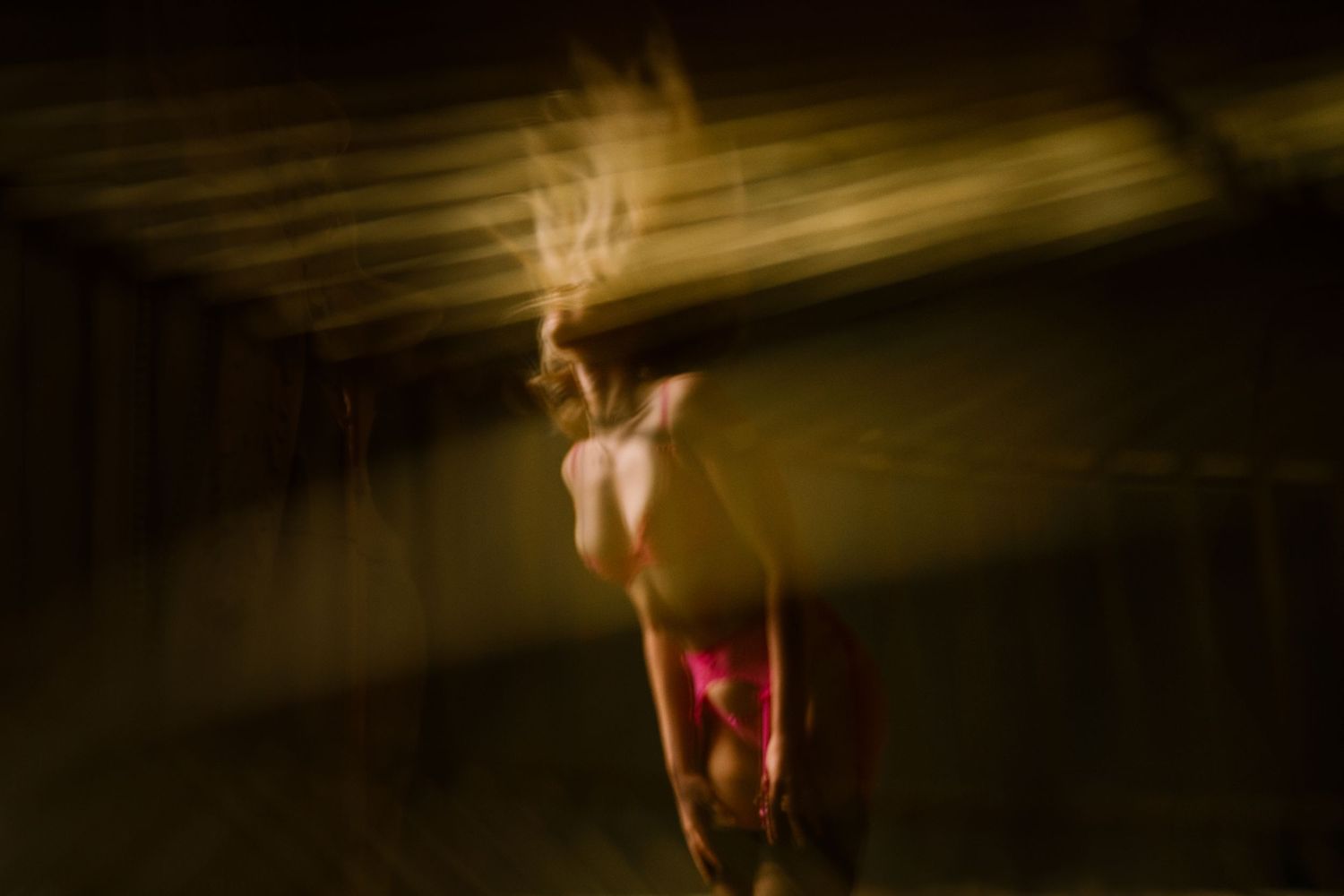 Blurred motion art photo of a dancer in pink under dramatic golden light creating an ethereal, ghostly effect.