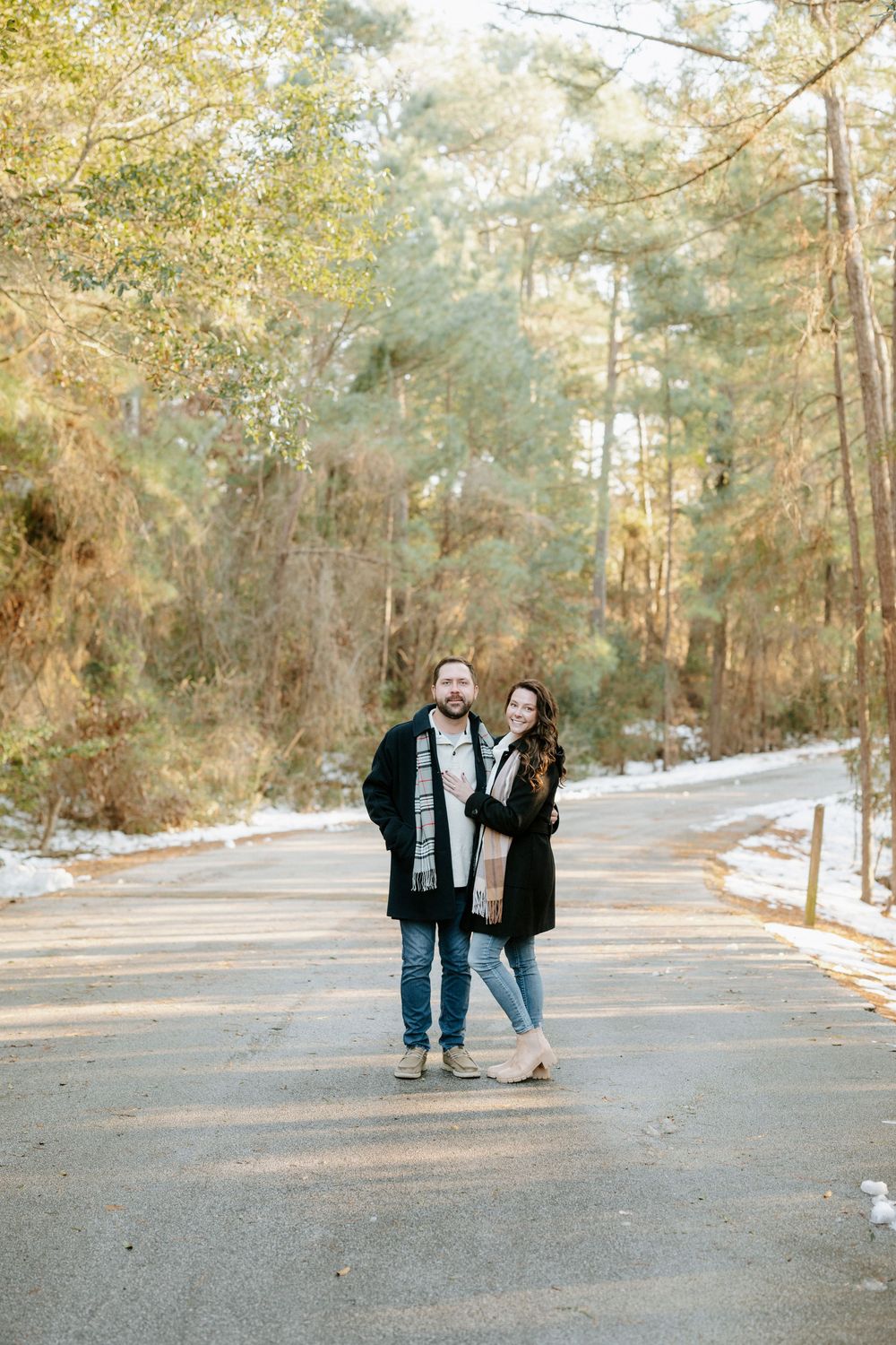 A couple takes a romantic winter stroll together along a snowy path lined with tall pine trees.