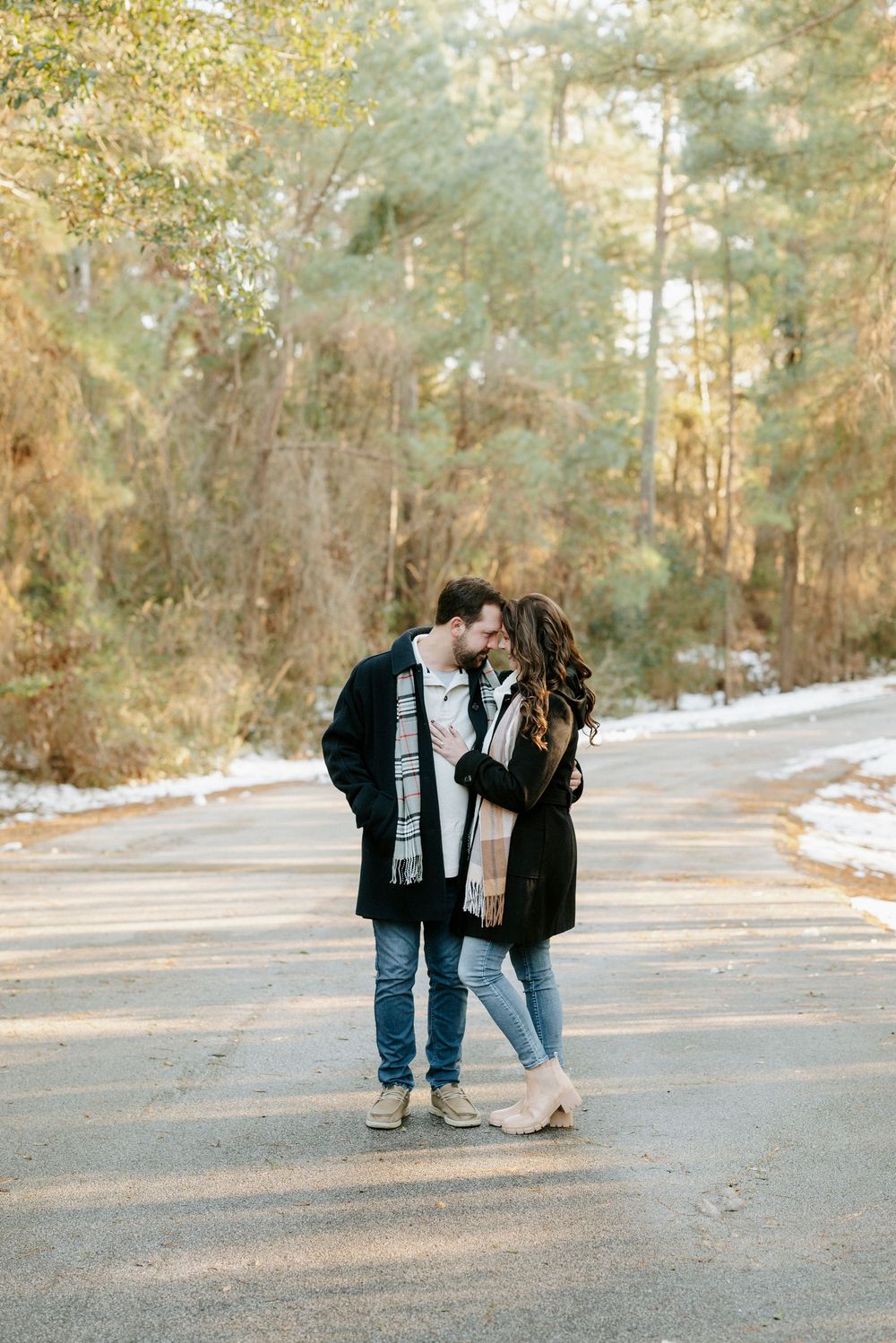 A romantic couple in winter attire shares tender moments on a sunlit forest path.