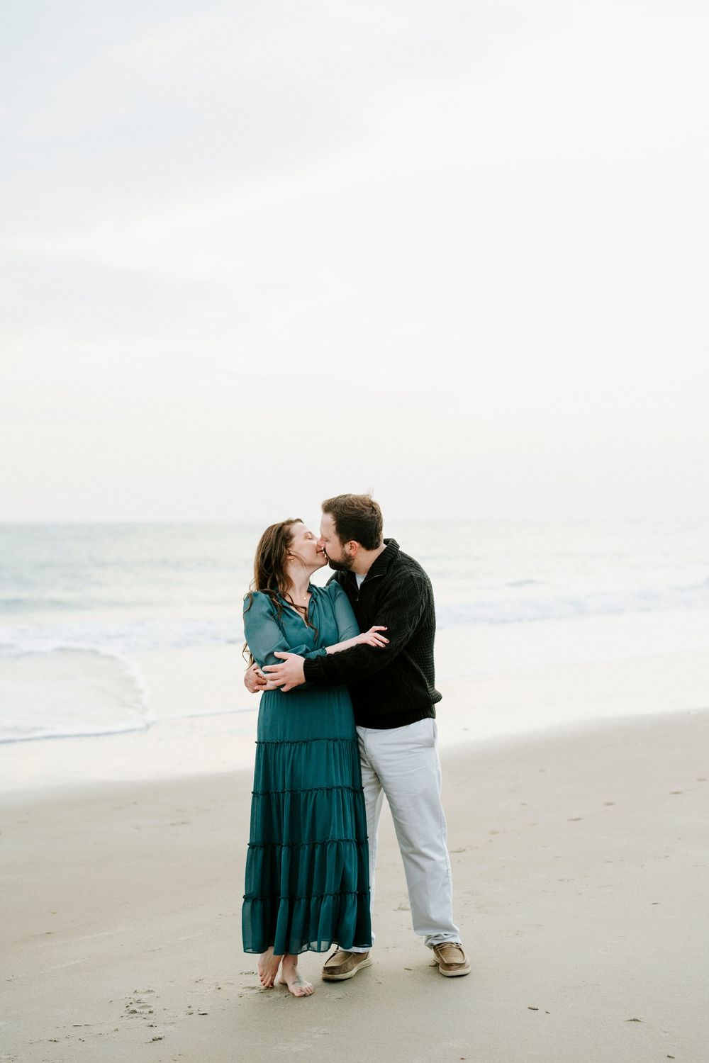 A romantic couple shares intimate moments on a cloudy beach while wearing coordinated casual attire.