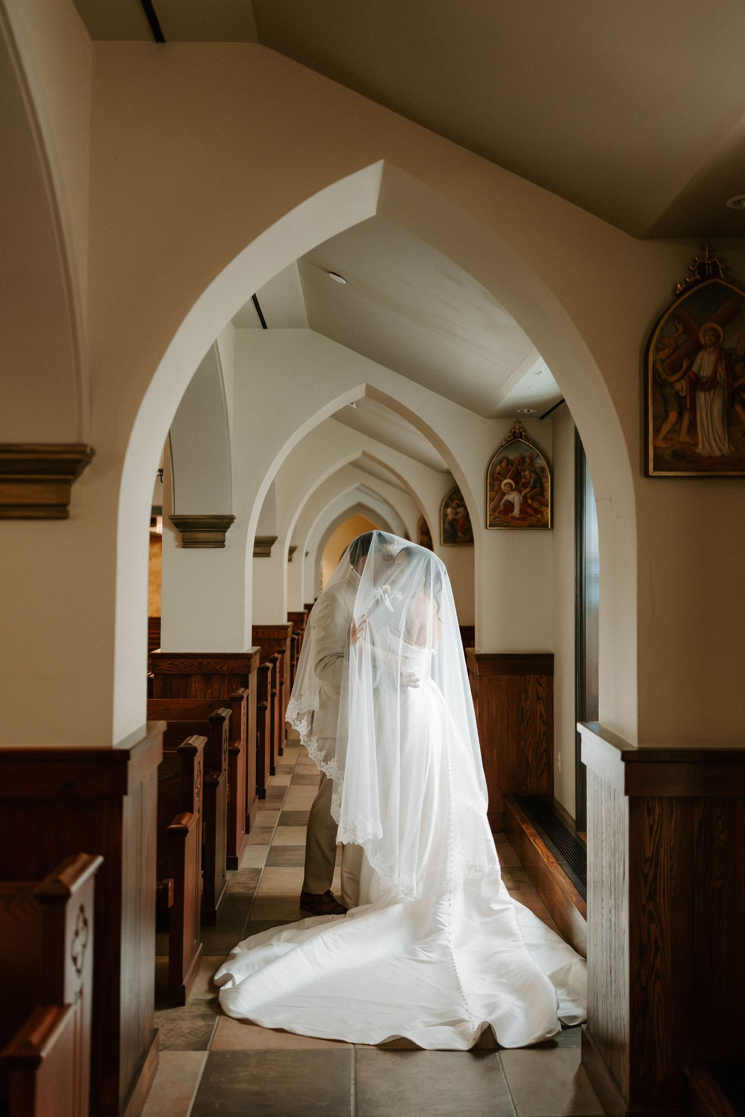 Bride and groom share an intimate moment under a flowing veil in sunlight.