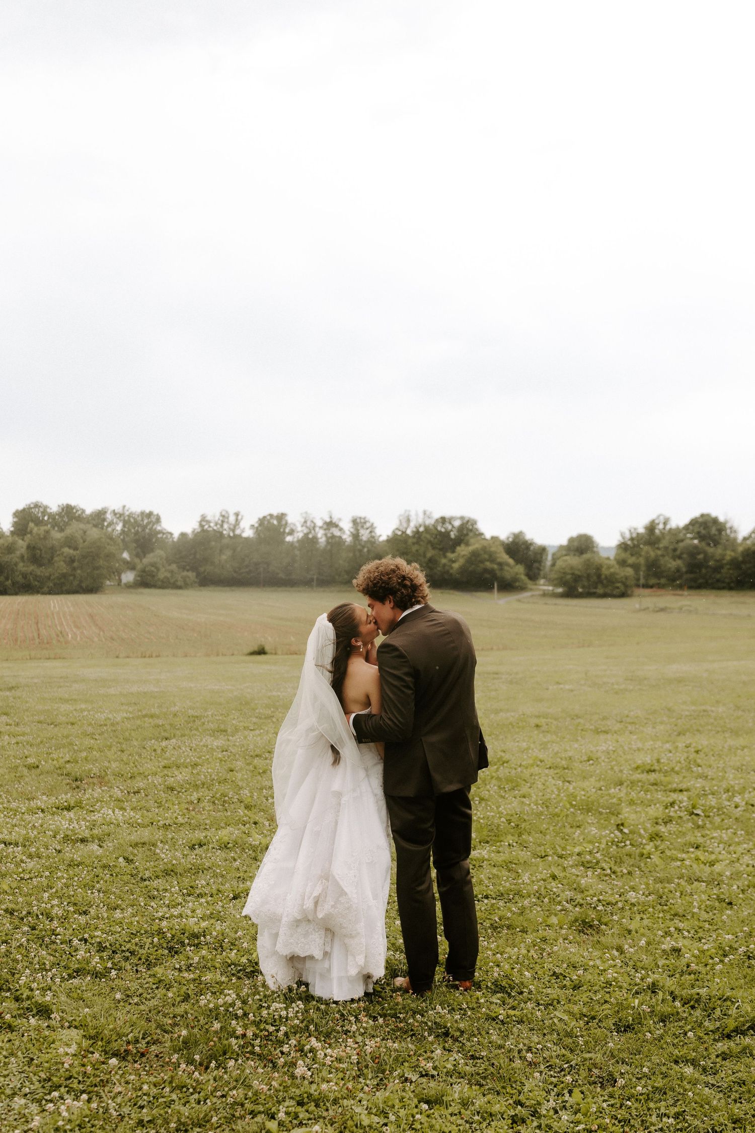 Bride and groom share an intimate moment under a flowing veil in sunlight.