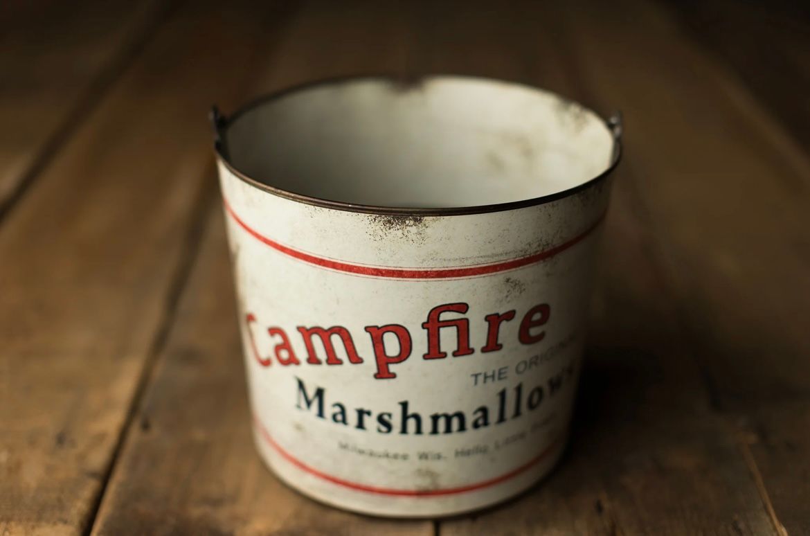 Vintage white ceramic jars with red lettering sit in a row on a rustic wooden surface in warm lighting.