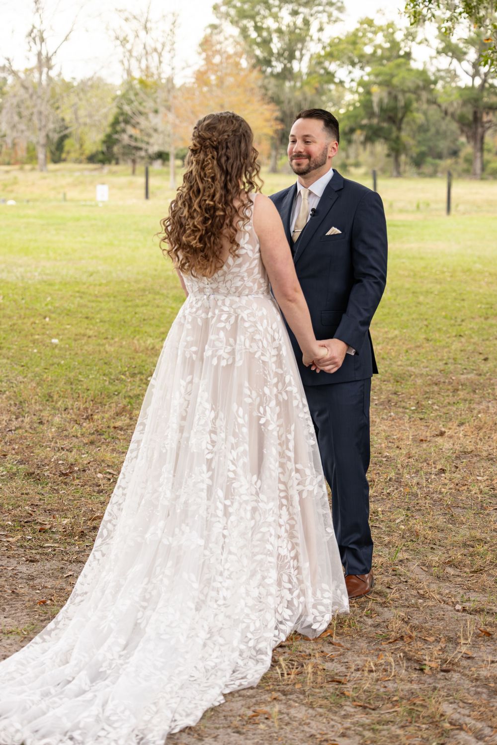 A couple holds hands during their wedding photoshoot, with the bride wearing an elegant lace gown with a flowing train.