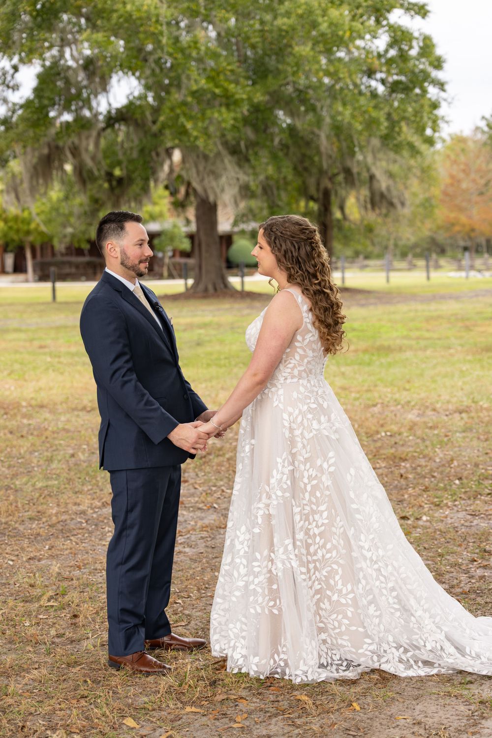 A couple in wedding attire holds hands in a park setting with Spanish moss draped oak trees in the background.