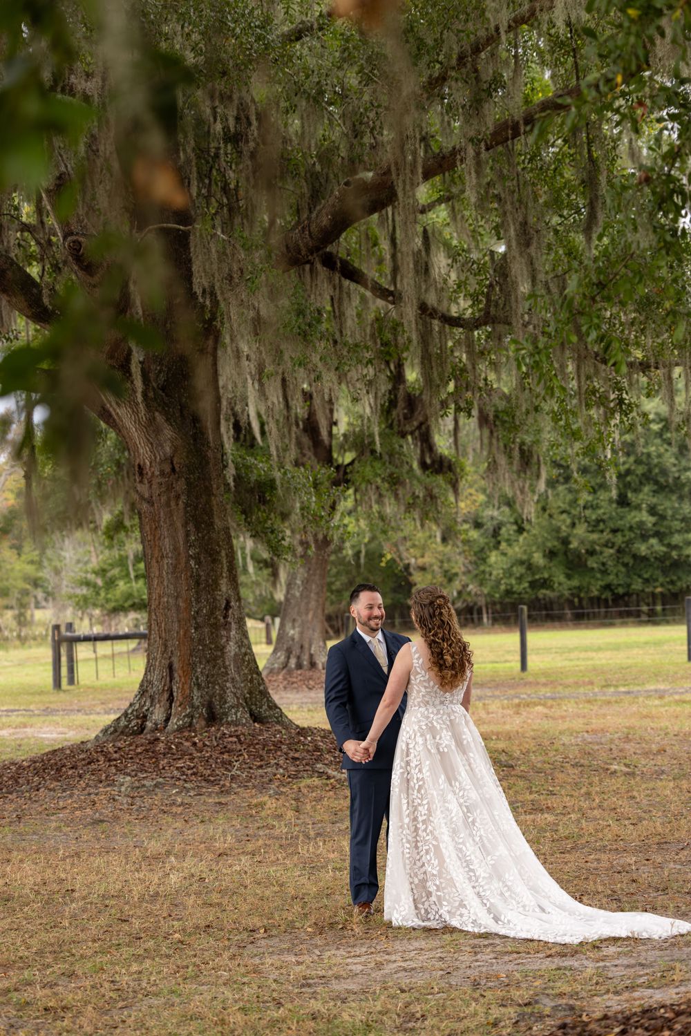 A couple shares a romantic moment under Spanish moss-draped oak trees in a serene outdoor setting.