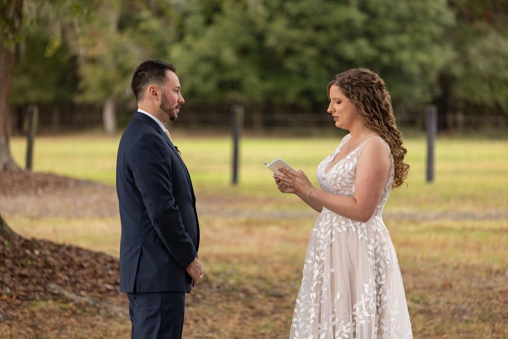 A couple in wedding attire stands together in a wooded outdoor setting during their special day.