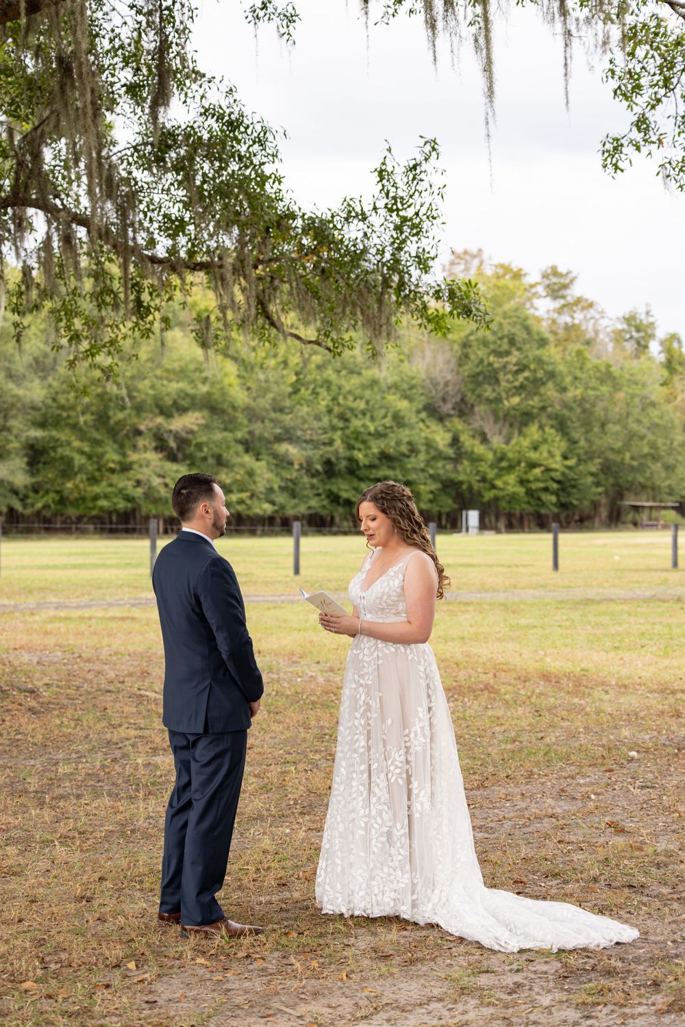 A couple shares their first look moment in a beautiful outdoor setting with Spanish moss draped trees.
