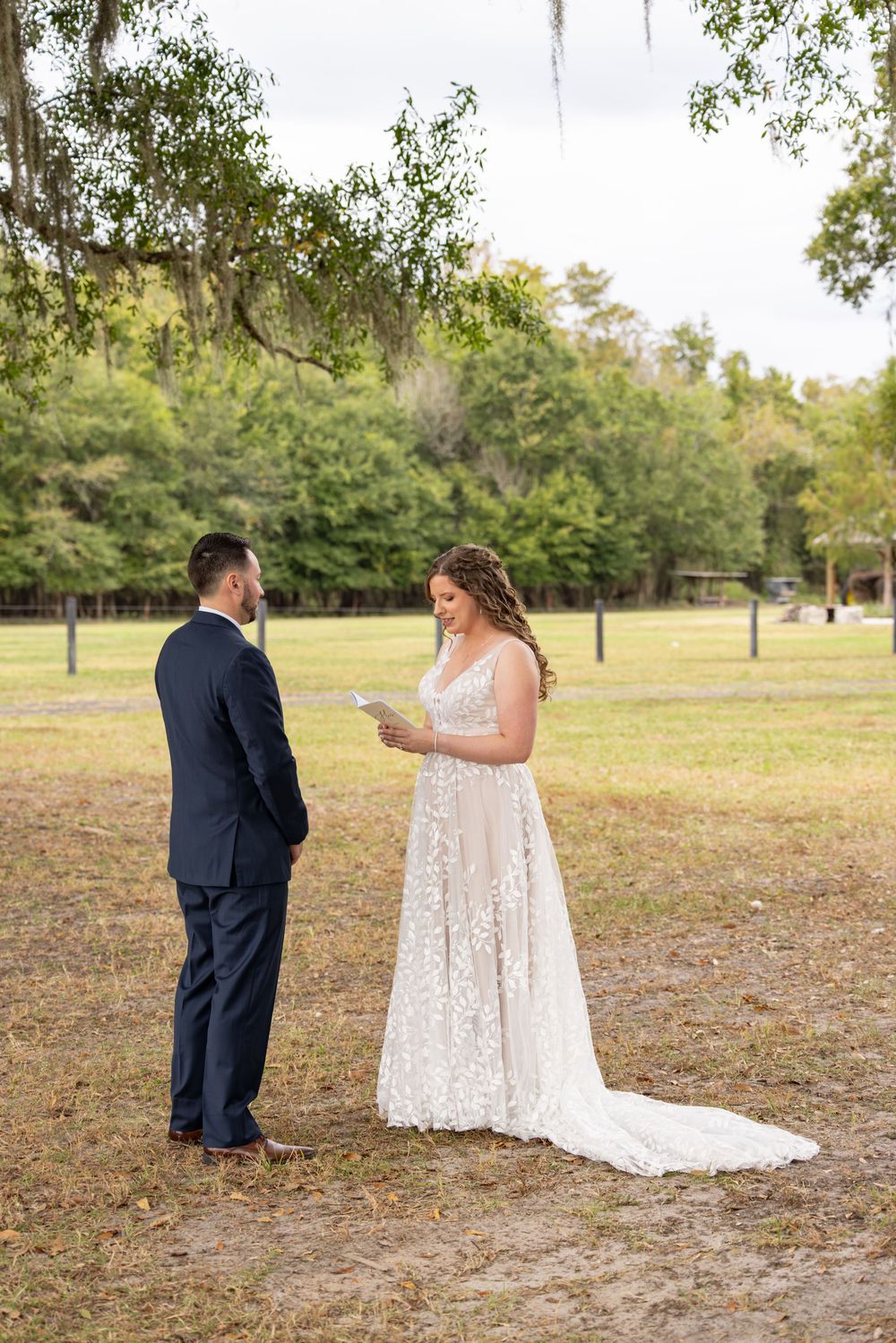 A couple exchanges vows during an outdoor wedding ceremony under Spanish moss draped trees.