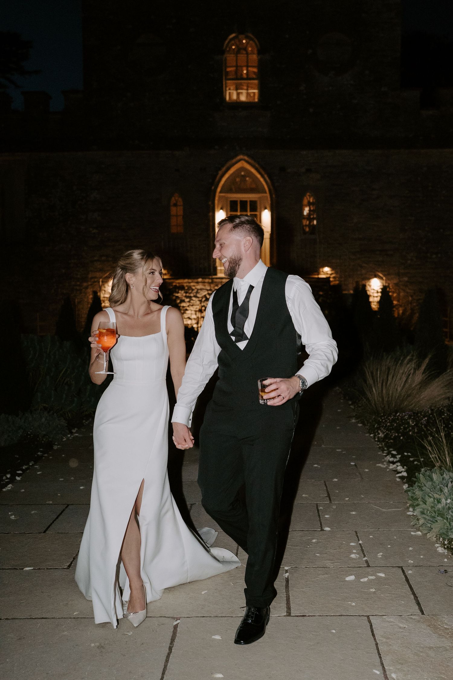 bride and groom walking and smiling at each other holding cocktails at ivy lodge wedding in cirencester