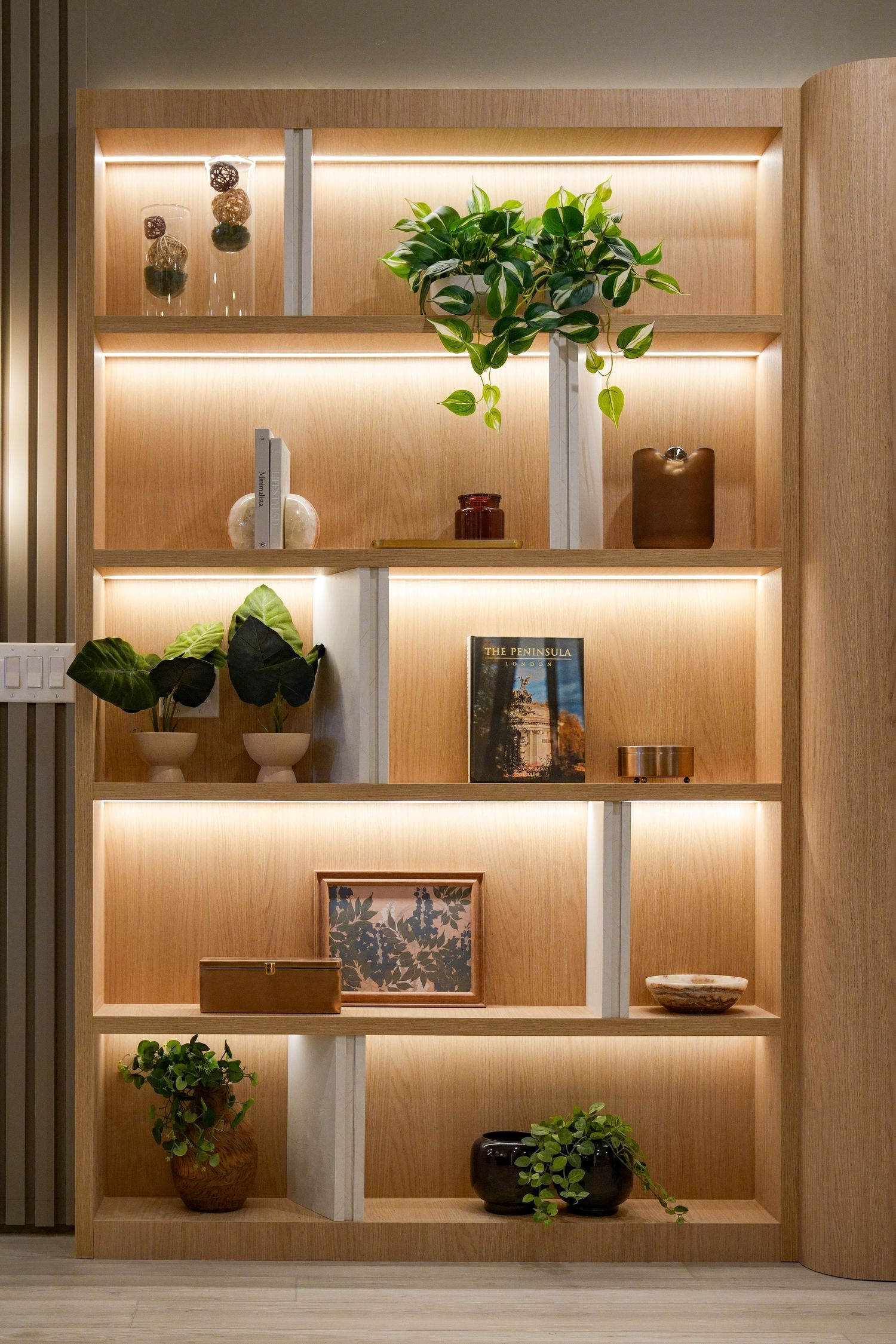 Modern built-in shelving unit with warm lighting showcases decorative plants and objects against light wood paneling.