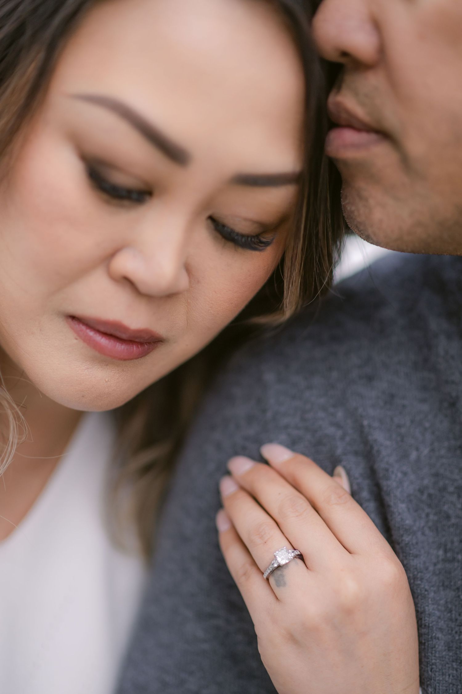 Close up engagement photo showing couple in romantic poses with diamond ring and gray sweater details.