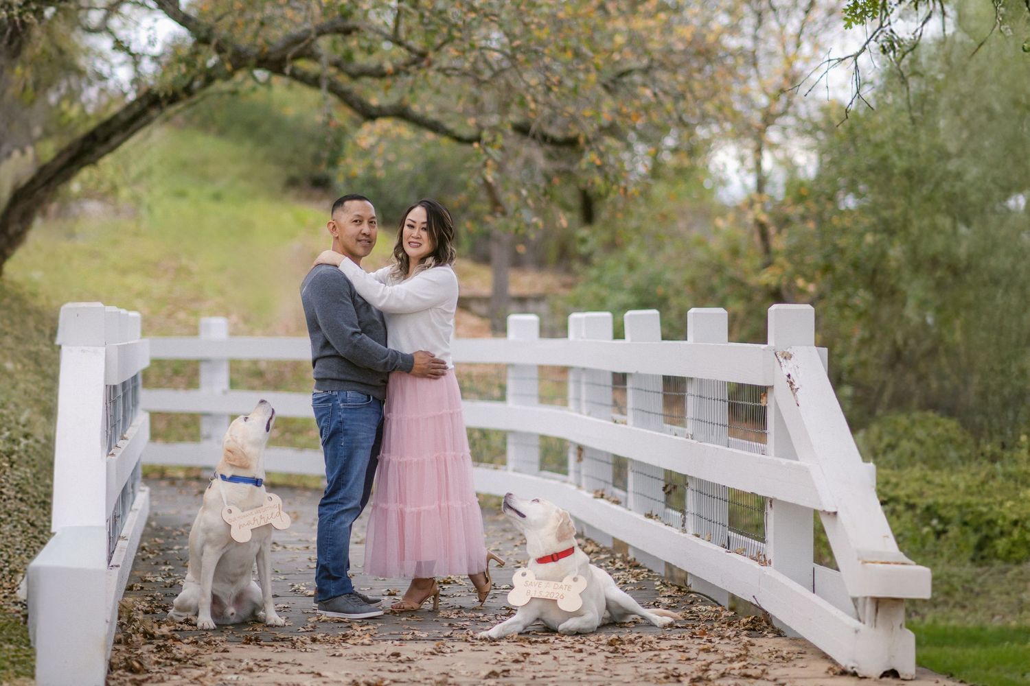 A couple sits together on a rustic white fence surrounded by autumn trees in a romantic outdoor setting.
